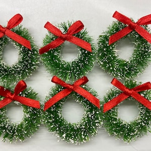 May include: Six small green wreaths with red bows. The wreaths are made of a fluffy material that looks like pine needles. The bows are tied in a simple knot.