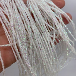 May include: White iridescent yarn with a fine glitter finish. The yarn is soft and shimmery, perfect for adding a touch of sparkle to any project.