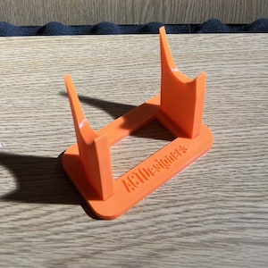 Può includere: Supporto in plastica arancione con il testo "ACTdesigner's" stampato sulla base.