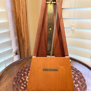 May include: A wooden Seth Thomas metronome with a pyramid shape. The metronome has a brass face with tempo markings and a swinging pendulum. The base of the metronome has a small metal plate with the name "Seth Thomas".
