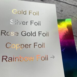 May include: A white card displays foil color options: Gold, Silver, Rose Gold, Copper, and Rainbow. The text is in a metallic finish. A second card with a rainbow foil effect is visible.