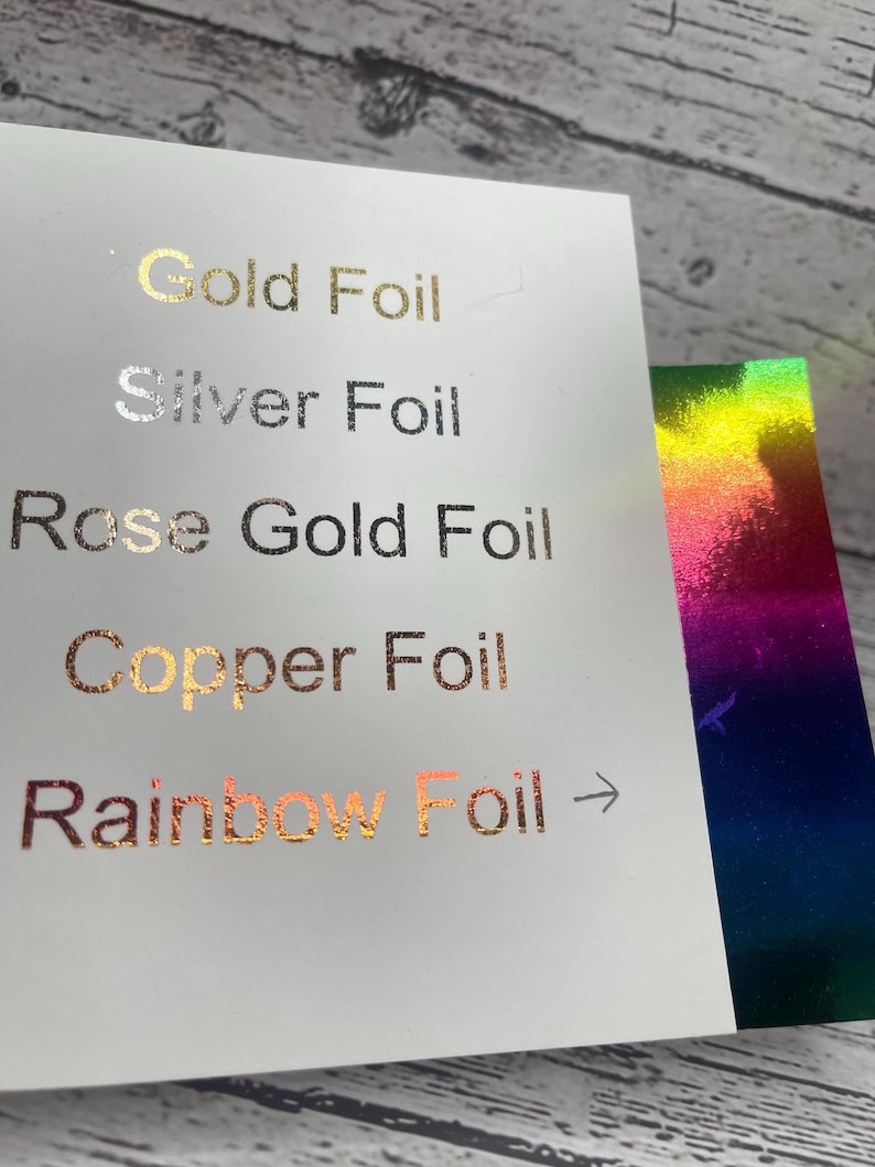 May include: A white card displays foil color options: Gold, Silver, Rose Gold, Copper, and Rainbow. The text is in a metallic finish. A second card with a rainbow foil effect is visible.