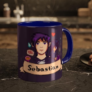 May include: A dark blue ceramic mug featuring a pixel art illustration of a character with purple hair. Below the character, a beige banner displays the name Sebastian in black pixelated text. A small red heart icon floats above the character.