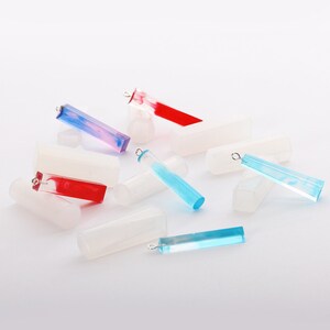 May include: Assortment of colorful resin pendant blanks with silver jump rings. The blanks are rectangular and have a marbled effect. Some are blue, red, and pink.