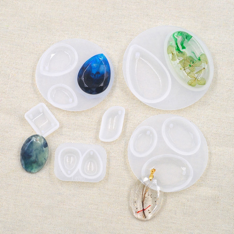 May include: A set of six clear silicone moulds for making jewellery pendants. The moulds are shaped like teardrops, ovals, and a rectangle. The moulds are on a white surface.
