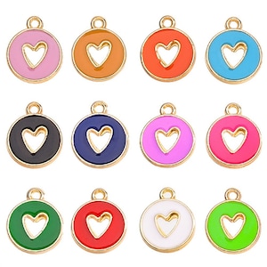 Könnte beinhalten: Zwölf goldfarbene Metall-Anhänger mit einem herzförmigen Ausschnitt. Jeder Anhänger ist in einer anderen Farbe lackiert: rosa, orange, rot, blau, schwarz, marineblau, pink, magenta, grün, rot, weiß und lindgrün.