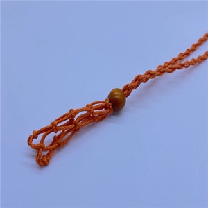 May include: Orange macrame cord necklace with a brown wooden bead.