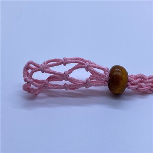 May include: A pink crocheted net with a brown wooden bead attached to the end.