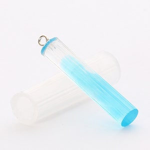 May include: A clear blue resin pendant with a silver jump ring. The pendant is shaped like a cylinder and has a smooth, polished finish.