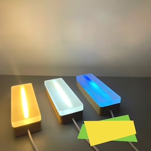 May include: Three rectangular light fixtures with different coloured lights. The lights are encased in clear acrylic and sit on wooden bases. The lights are yellow, white, and blue.