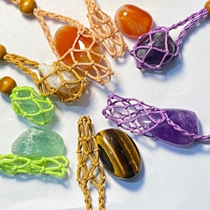 May include: A collection of seven colorful crystal stones, each encased in a crocheted net bag. The stones include amethyst, carnelian, tiger's eye, clear quartz, green aventurine, and two other stones.