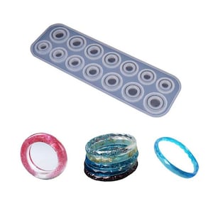 May include: A silicone mould with 15 circular ring shapes for making resin jewellery. The mould is light blue and has a smooth surface. There are three examples of finished resin rings in different colours and styles.