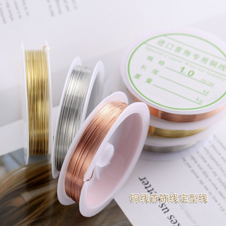 Puede incluir: Tres carretes de alambre para la elaboraci&oacute;n de joyas. Los carretes est&aacute;n etiquetados como "Alambre de cobre especial para joyer&iacute;a" y "1,0 mm". El alambre es dorado, plateado y cobre.