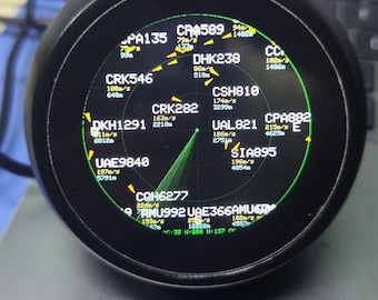 May include: A circular black digital display screen showing a radar-style interface with green text and graphics. The screen features various flight codes like CRK546, DHK238, and UAL821, along with numerical data for speed in m/s and altitude in meters.