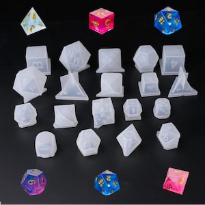 May include: A set of 18 clear silicone molds for making dice. The molds are in various shapes, including a cube, a pyramid, a tetrahedron, and a dodecahedron. There are also several dice in the image, including a pink and blue dice.