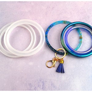May include: Three silicone bangle molds in white, and three finished resin bangles in blue, green, and purple with gold glitter. The resin bangles are attached to a gold key chain with a blue tassel.