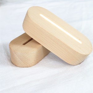 Könnte beinhalten: Zwei ovale Holzsockel mit integriertem LED-Lichtstreifen. Die Sockel sind aus hellem Holz und haben eine glatte Oberfläche.