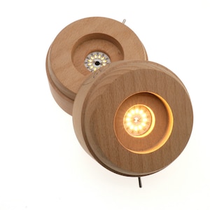 Op de afbeelding: Twee houten bases met een ronde uitsparing, elk met een kleine LED-lichtbron. De lampen zijn aan en verlichten de omgeving.