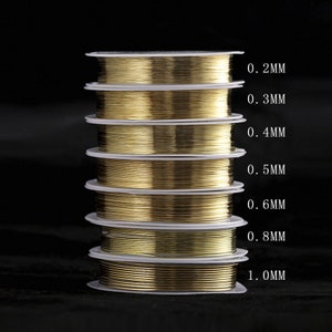 Puede incluir: Una pila de carretes de alambre de color dorado, cada carrete est&aacute; etiquetado con un grosor de alambre diferente en mil&iacute;metros, que van de 0,2 mm a 1,0 mm.