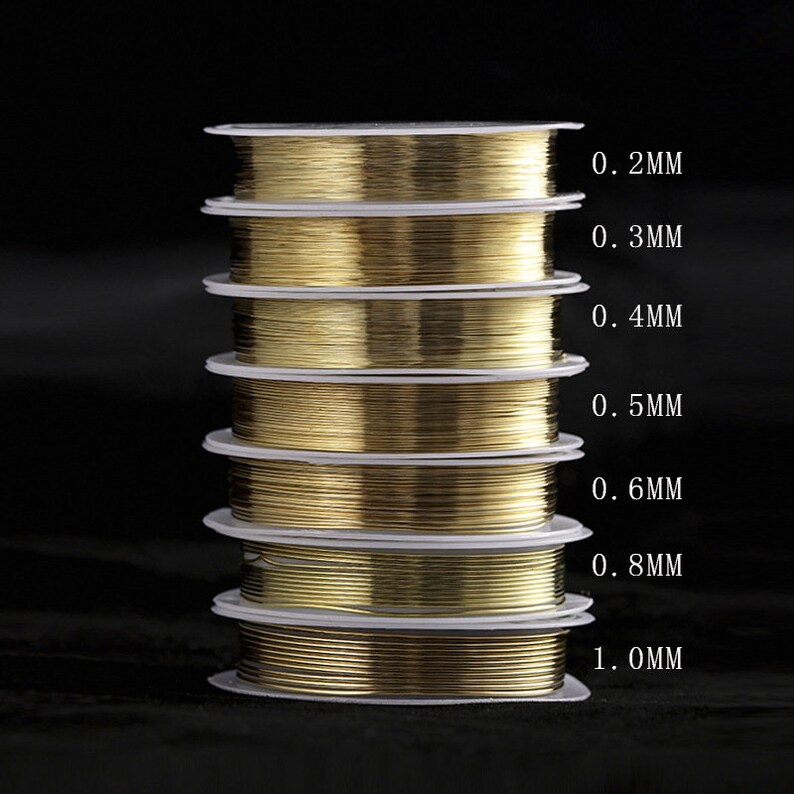 Puede incluir: Una pila de carretes de alambre de color dorado, cada carrete est&aacute; etiquetado con un grosor de alambre diferente en mil&iacute;metros, que van de 0,2 mm a 1,0 mm.