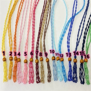 May include: Sixteen different colored cords with wooden beads at the end. The cords are all the same length and are arranged in a row. The cords are all different colors, including yellow, orange, pink, red, brown, blue, and green.