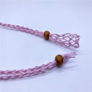 May include: A pink braided cord with wooden beads at each end. One end has a small pink crocheted net bag.