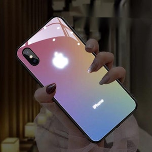 Puede incluir: Una funda transparente para teléfono con un degradado de rosa, naranja, amarillo y azul. La funda tiene un logotipo de Apple blanco brillante y la palabra "iPhone" impresa en la parte posterior.