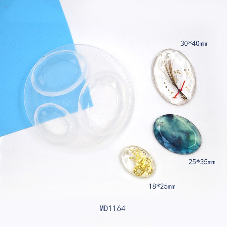 May include: A clear silicone mould with three oval-shaped cavities. The mould is designed for making resin pendants. Three resin pendants are shown next to the mould, each with a different design. The pendants measure 18x25mm, 25x35mm, and 30x40mm.