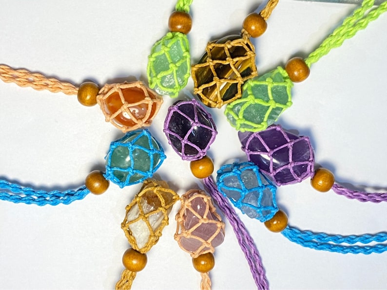 May include: A collection of colorful crystal stones wrapped in macrame string. Each stone is a different color and shape, and they are all strung together with a wooden bead.