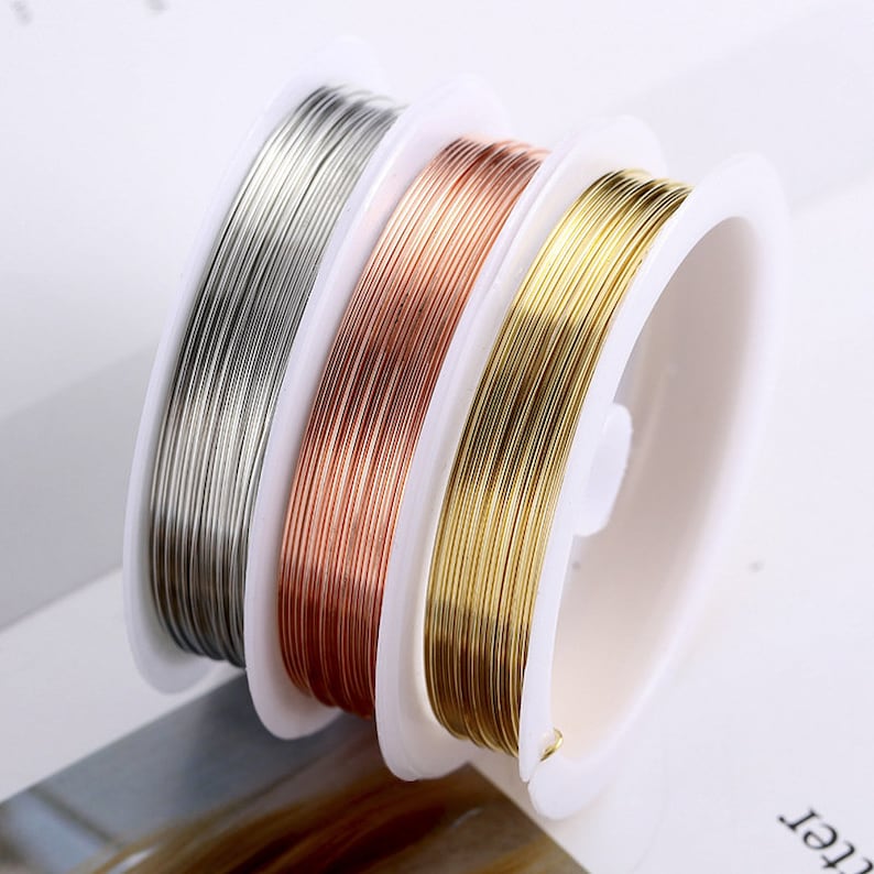 Puede incluir: Tres carretes de alambre para la elaboraci&oacute;n de joyas. Los carretes son de pl&aacute;stico blanco y el alambre es plateado, oro rosa y oro.