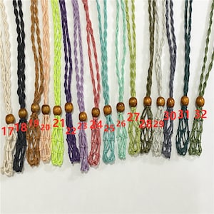 May include: A collection of 16 macrame cord necklaces with wooden beads. The cords are in various colors, including black, brown, pink, green, purple, blue, and gray. The necklaces are numbered 17 through 32.