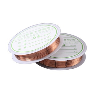 Puede incluir: Dos carretes de alambre de cobre para la fabricaci&oacute;n de joyas. Los carretes est&aacute;n etiquetados con el texto "Jewelry Copper Wire for Jewelry" y el grosor del alambre en mil&iacute;metros. El primer carrete est&aacute; etiquetado "0.4 mm" y el segundo carrete est&aacute; etiquetado "4 mm".