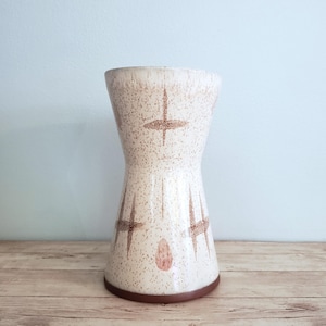 May include: A white ceramic vase with a brown geometric pattern. The vase has a wide mouth and a narrow base.