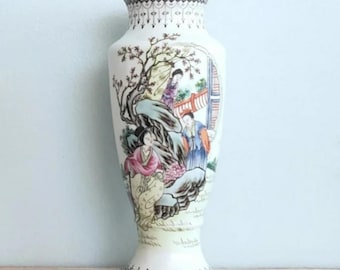 May include: White ceramic vase with a floral design and a scene of people in traditional clothing. The vase has a wide base and a narrow neck.