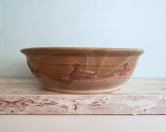 May include: A large, brown ceramic bowl with a speckled glaze. The bowl features a design of three brown ducks in a row.