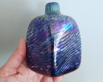 May include: A small, iridescent glass vase with a square shape and a swirling, blue and purple pattern.