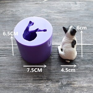 May include: A purple silicone mold and a small dog figurine. The mold is cylindrical, 6.5 cm tall and 7.5 cm wide, with a dog-shaped cavity. The dog figurine is white with black markings, 6 cm tall and 4.5 cm wide.