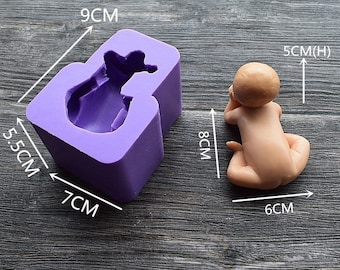 May include: A purple silicone mold, 9cm x 7cm x 5.5cm, shaped like a baby, next to a finished baby figurine, 8cm long and 6cm wide. The baby figurine is light brown with its hands near its face.