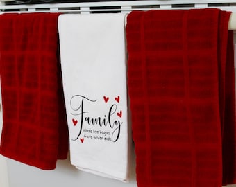 May include: Two red kitchen towels hanging on a rack with a white kitchen towel in the middle. The white towel has the text "Family where life begins & love never ends" with red hearts.