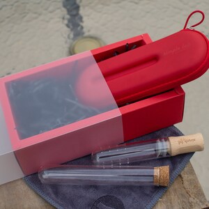 May include: A red gift box with a red carrying case for a set of glass straws. The carrying case has the text "Simple-Lab" printed on it. The straws are in clear glass tubes with wooden tops and cork bottoms.