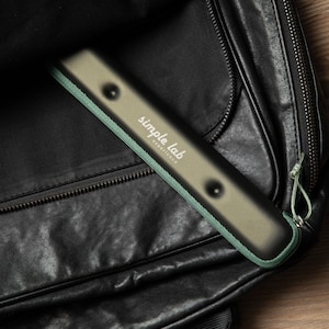 Könnte beinhalten: Eine schwarze Ledertasche mit Reißverschluss und einem grün-beigen Beutel mit dem Text "simple lab headphones" im Inneren.