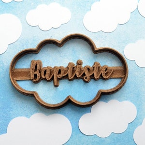 Può includere: Un tagliapasta di plastica marrone a forma di nuvola con il nome "Baptiste" scritto in un carattere decorativo.