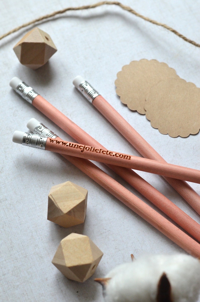 Puede incluir: Tres l&aacute;pices de madera con gomas blancas y una banda plateada. Los l&aacute;pices son rosados y tienen el texto "www.unejoliefete.com" grabado en ellos. Los l&aacute;pices est&aacute;n sobre una superficie blanca con formas geom&eacute;tricas de madera y un c&iacute;rculo de papel marr&oacute;n.