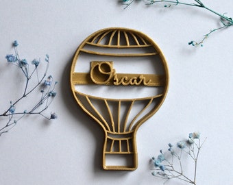 May include: Gold-colored hot air balloon cookie cutter with the name "Oscar" inscribed on the side.