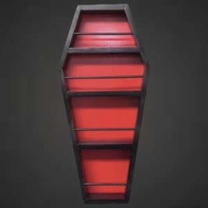 May include: A coffin-shaped shelf with a black frame and a red interior. The shelf has multiple horizontal shelves for displaying items. The design is gothic and unique, perfect for adding a spooky touch to any room.