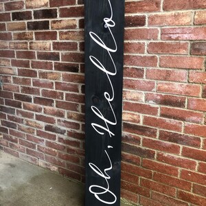 May include: A black wooden sign with the words "Oh, hello" written in white cursive script.