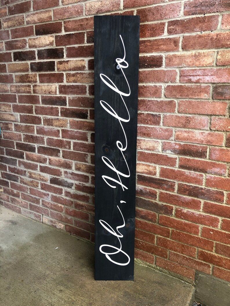 May include: A black wooden sign with the words "Oh, hello" written in white cursive script.