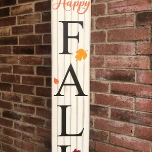 May include: A white wooden sign with the words "Happy Fall Y'all" in orange and black lettering. The sign features a pumpkin and fall leaves.