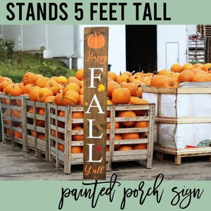 May include: A wooden sign with the words "Happy Fall Y'all" painted on it. The sign is decorated with a pumpkin and leaves. It stands 5 feet tall and is displayed in front of a pile of pumpkins.