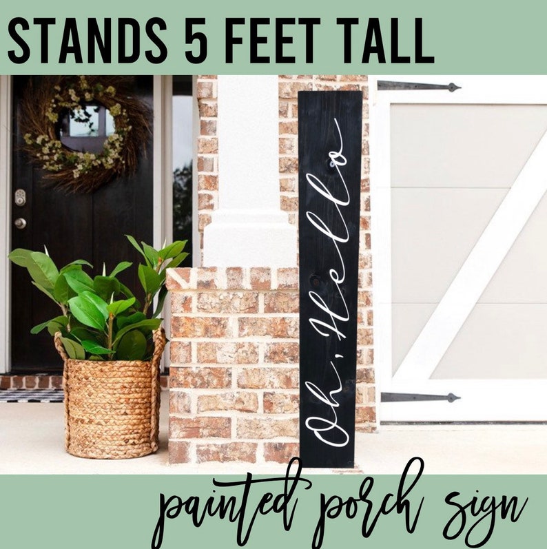 May include: Black wooden porch sign with white cursive lettering that reads "Oh, Hello". The sign is 1.5 metres tall and is leaning against a brick wall.
